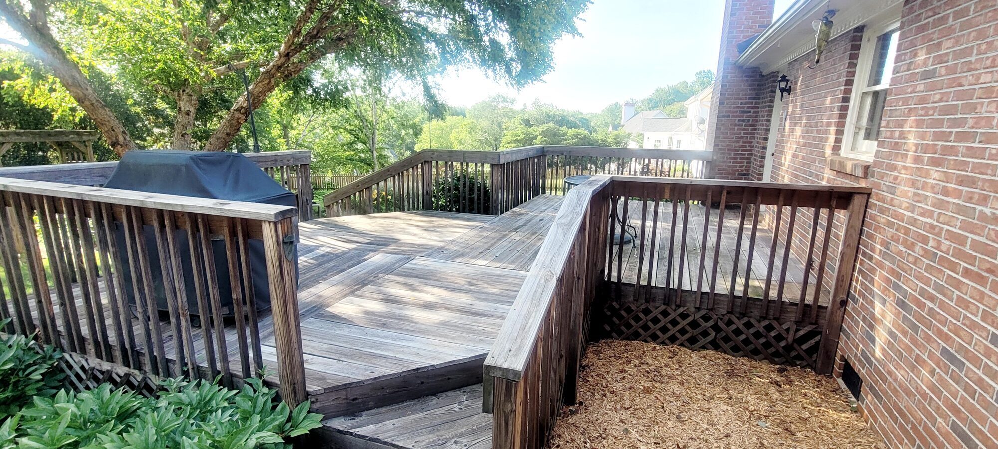 A weathered gray wood deck before cleaning and staining, next to a brick home
