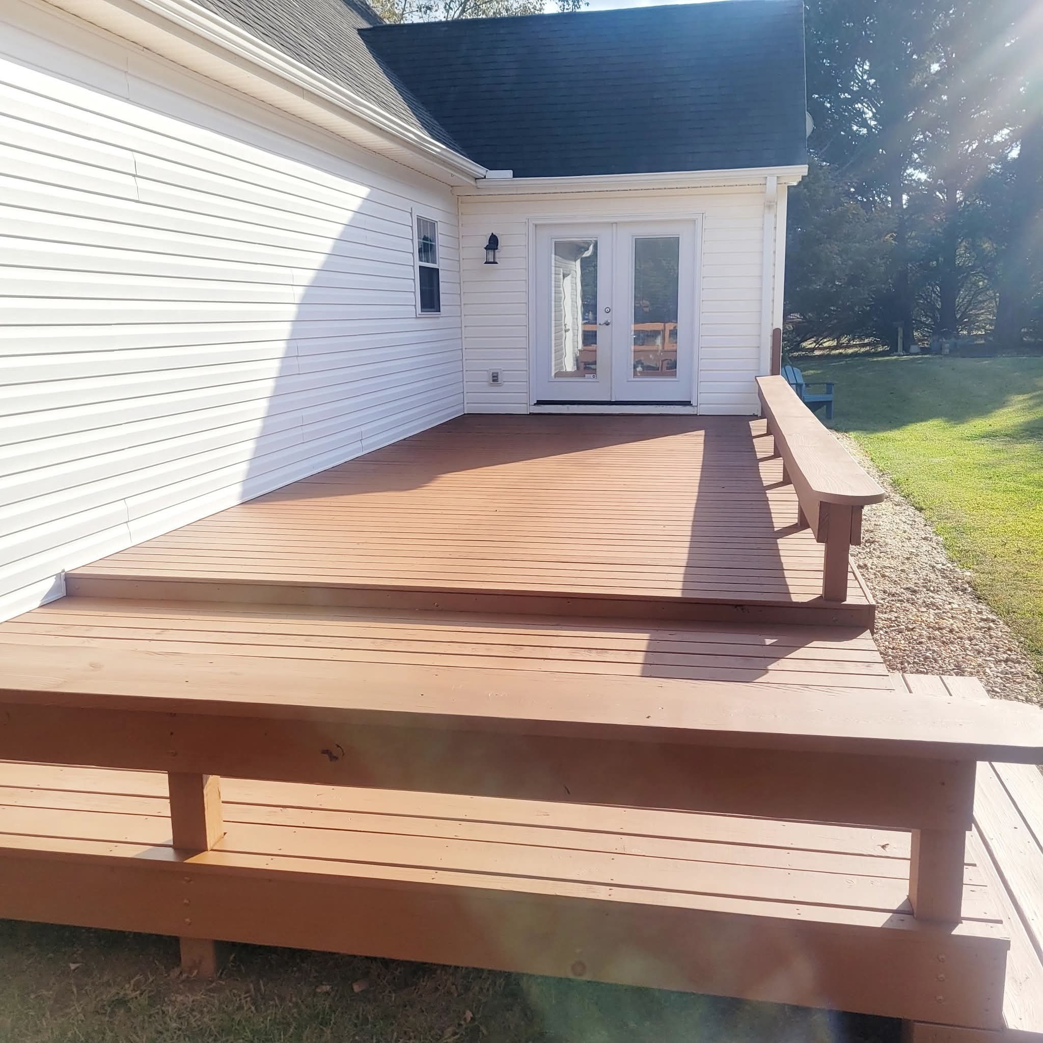 A finished deck stained a warm reddish brown next to a home with white siding and French doors