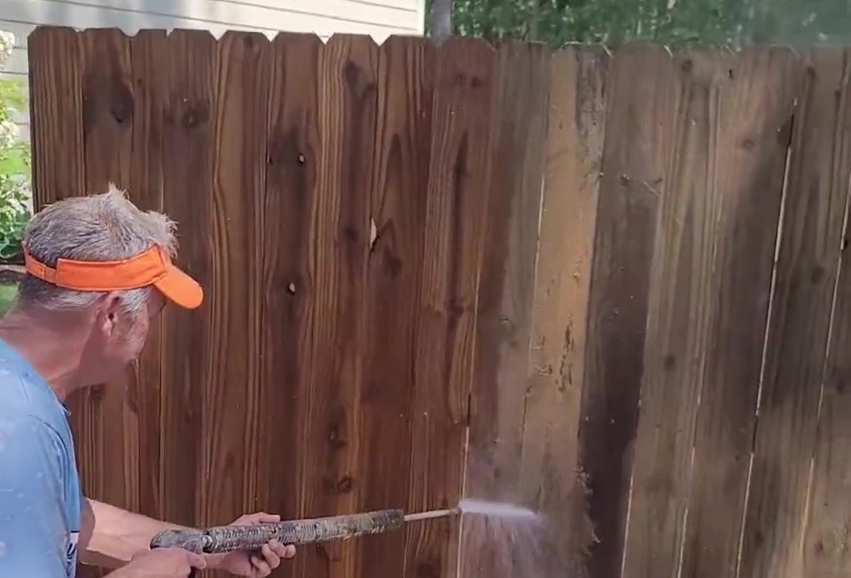 A crew member pressure washing years of dirt and mildew off a wood privacy fence